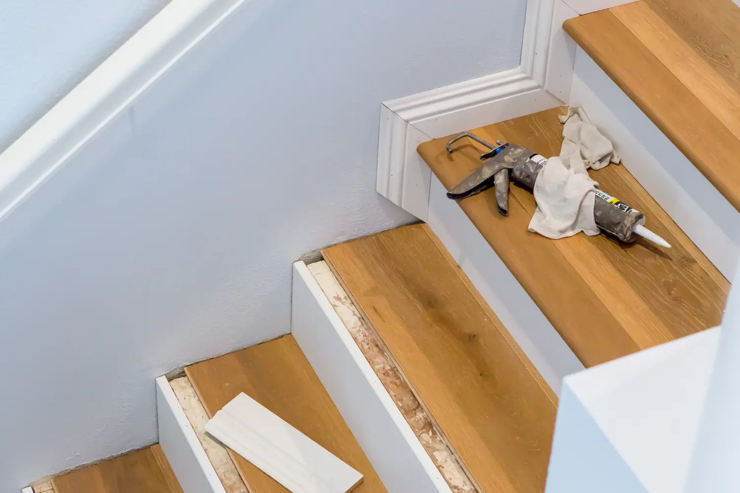 Hartholzbodenverlegung auf Treppen, Kartuschenpistole auf Stufe, Fußleisten werden gemessen